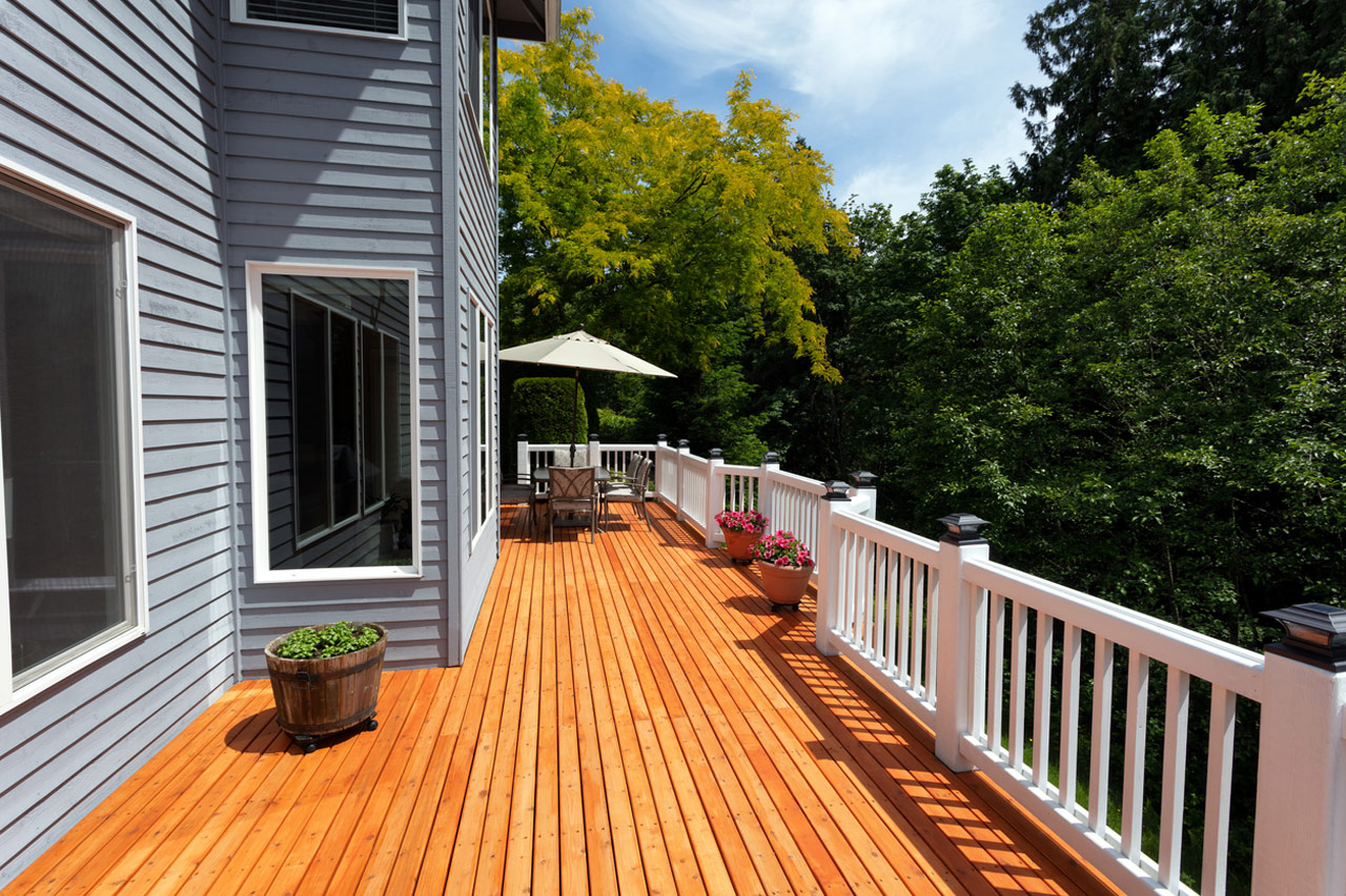 A residential deck featuring a sun umbrella and outdoor seating, surrounded by lush greenery, ideal for a relaxing outdoor living space.