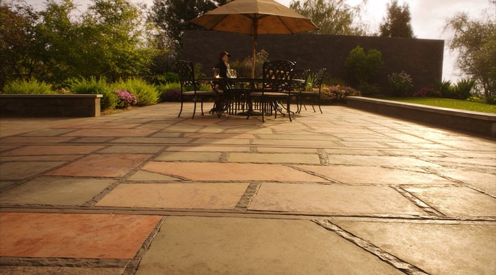 A luxurious stamped concrete patio with a dining set and umbrella, showcasing detailed workmanship in concrete construction for outdoor living.