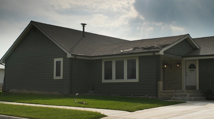 Storm-damaged residential home with missing shingles and yard debris