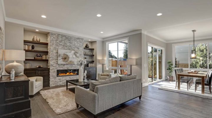Stylish living room with a stone fireplace and built-in shelves, adjoining a dining area with natural light, ideal for elegant home interiors.