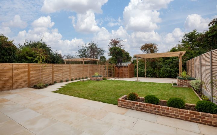 A beautifully landscaped garden featuring a pergola, well-manicured lawn, and a paved walkway, illustrating quality in garden remodeling and pergola construction.